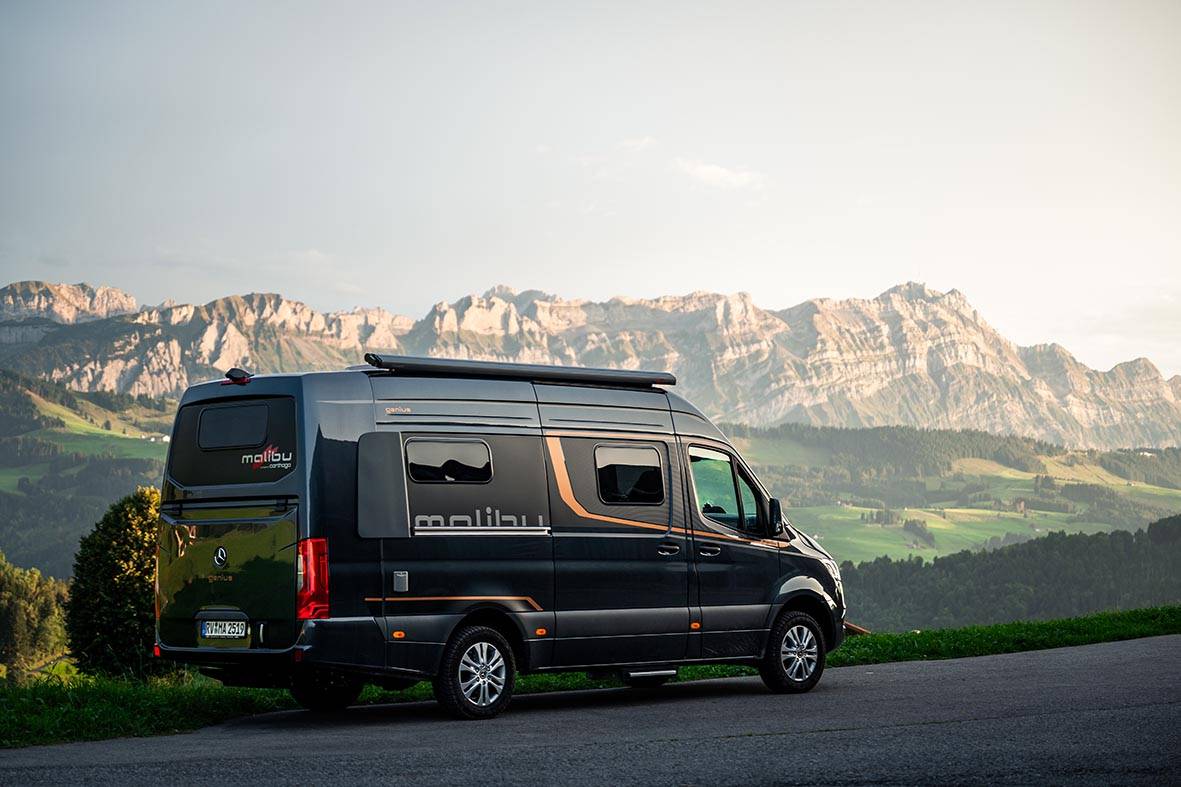 Malibu Genius 4x4 auf einer Bergstraße vor Alpenpanorama als Allrad-Camper für Reisen in den Bergen.