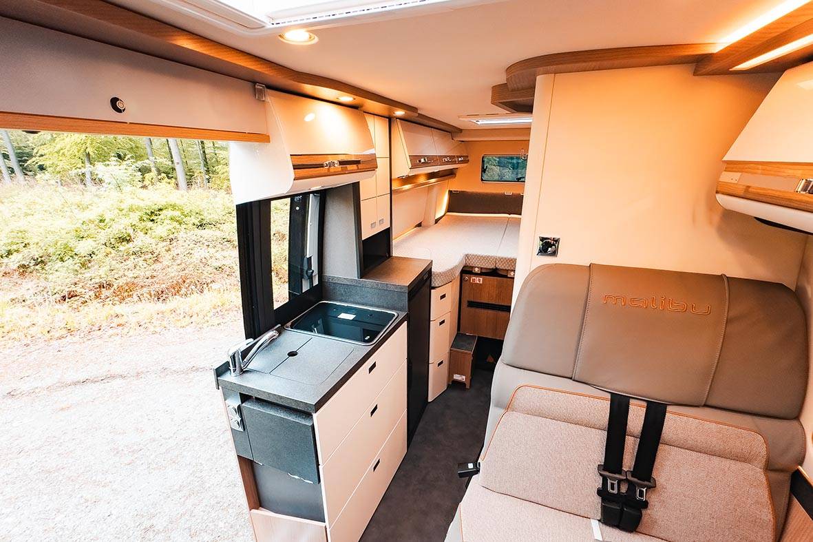 Innenraum des Malibu Genius 4x4 mit Küchenblock, Sitzplatz und Blick bis zum Schlafbereich.