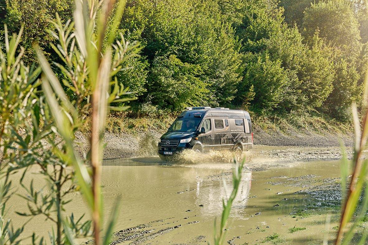 Malibu Genius Performance 4x4 fährt durch nasses Schottergelände mit Wasser und aufgewirbeltem Schlamm