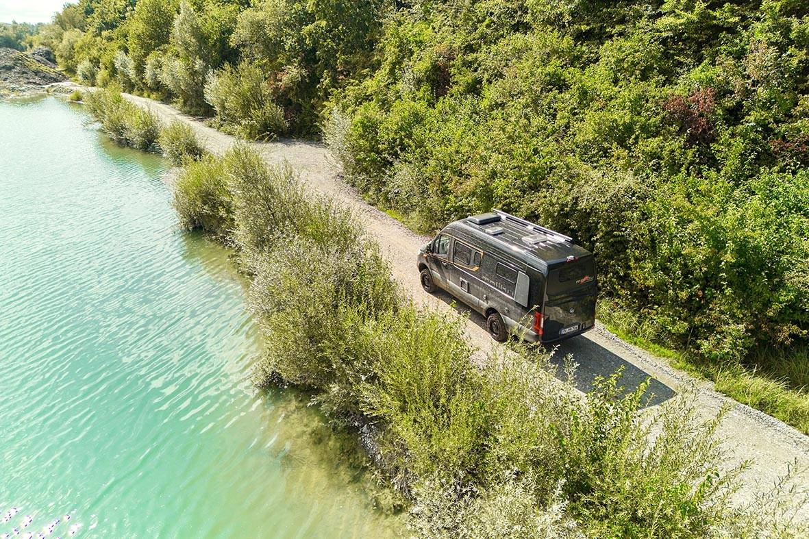 Malibu Genius Performance 4x4 von oben auf einem Schotterweg am See mit sichtbaren Dachaufbauten.