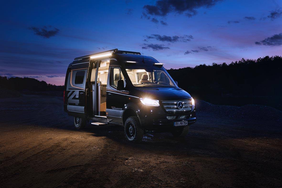 Malibu Genius 4x4 bei Nacht mit eingeschalteten Scheinwerfern, Innenraumbeleuchtung und geöffneter Schiebetür.