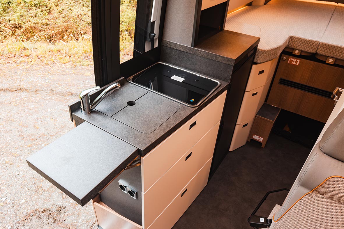 Küchenzeile im Malibu Genius 4x4 mit ausgezogener Arbeitsflächenerweiterung und Blick zu den Längsbetten.
