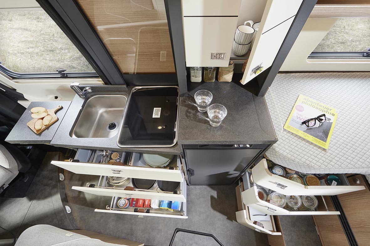 Küche im Malibu Genius 4x4 von oben mit geöffneten Schubladen, Spüle, Kocher und Stauraum.
