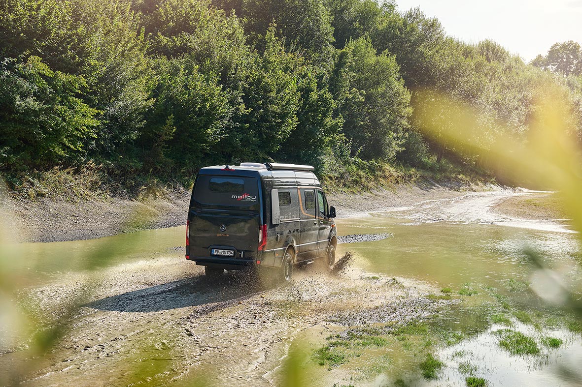 Heckansicht des Malibu Genius Performance 4x4 bei einer Fahrt durch Wasser und Schlamm im Offroad-Gelände.