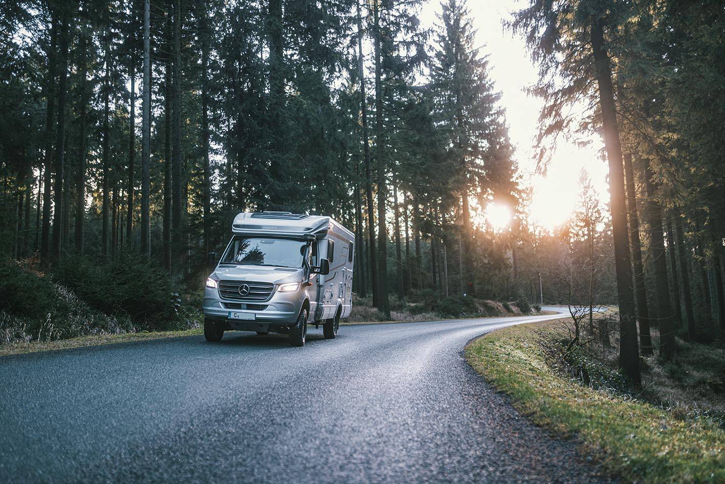 Der Hymer MLT 580 4x4 fährt am Abend auf einer asphaltiertes Straße durch den Wald.